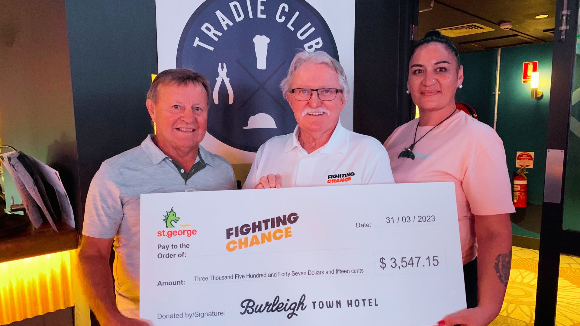 Ross Paterson, Neville Hedge and Ebony hold a large cardboard cheque donating money to Fighting Chance